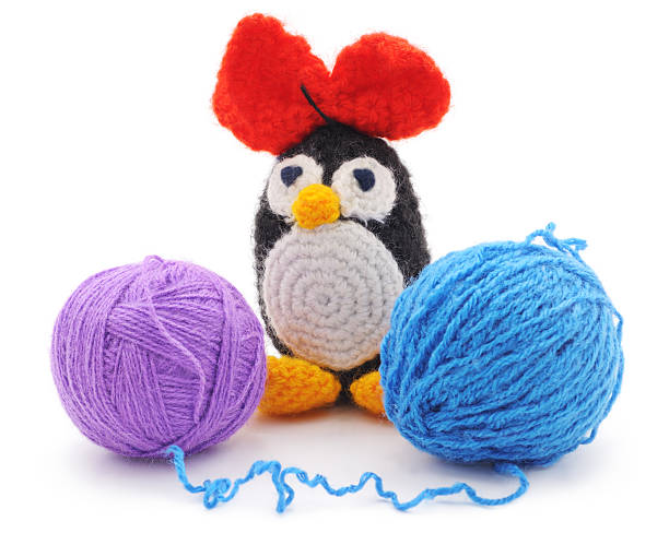Crocheted penguin with red heart ears beside purple and blue yarn—cute project from a crochet kit.

