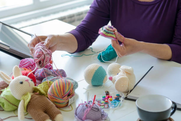 Woman crafting amigurumi at desk with yarn, tools, and finished pieces—ideal for a creative crochet kit.
