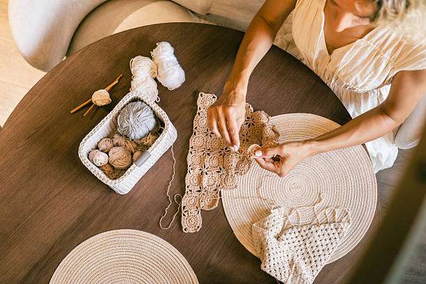 Overhead view of woman making lace with a Crochet Kit on a wooden table.